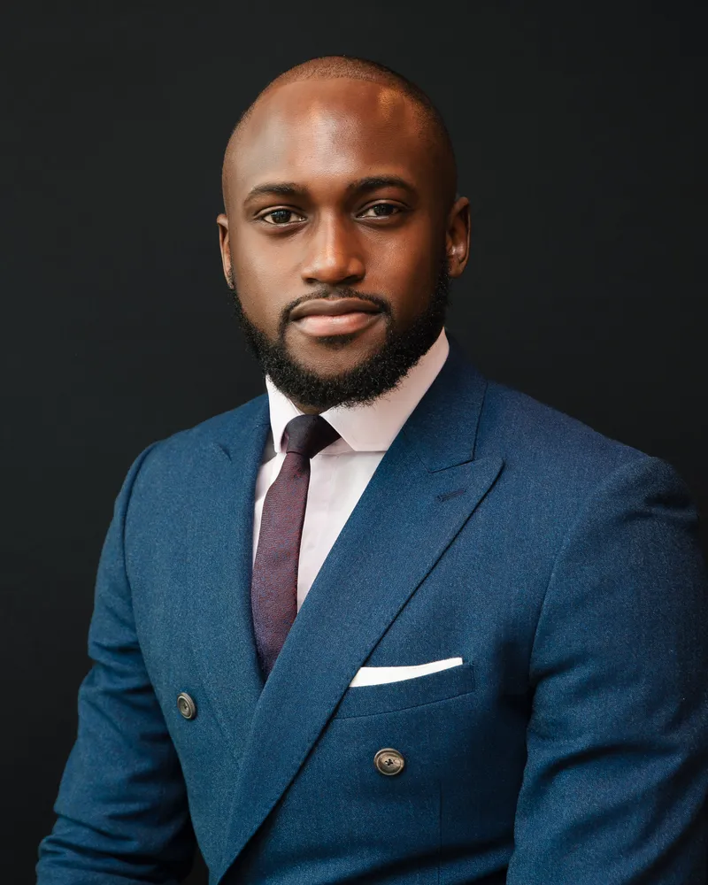 Benji Otieno, SkinBestie’s founder, in a navy double-breasted suit against a dark studio background
